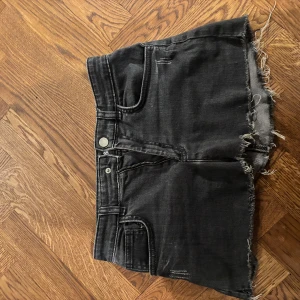 Svarta jeansshorts från Zadig & Voltaire - Snygga svarta jeansshorts från Zadig & Voltaire med fransiga kanter och en cool broderad detalj på bakfickan. Perfekta för en avslappnad stil med en touch av edge. De har en klassisk femficksdesign och en dragkedja framtill.