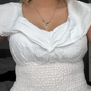 Vit volangblus - Säljer en söt vit blus med volangdetaljer och smockad midja. Blusen har korta ärmar och en v-ringad design både fram och i ryggen! 💞💞