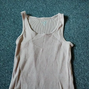 Beige ribbad linnetopp från Favourite - Säljer en beige ribbad linnetopp från Favourite i storlek S. Toppen är ärmlös med klassisk rund halsringning och har en mjuk, stretchig känsla. Perfekt att styla med jeans eller shorts för en chill look. Kan tvättas innan jag skickar det om du vill😄