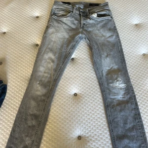 Ljusgråa jeans från dondup - Snygga ljusgrå jeans från Denim Group med skinny fit och slitning på ena benet. Klassisk femficksmodell med dragkedjegylf och diskreta detaljer. Perfekta för dig som gillar en modern och avslappnad stil.