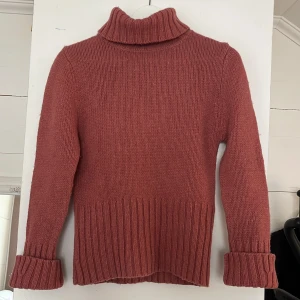 Rosa polotröja i merinoull från H&M - Säljer en chill polotröja från H&M i en snygg rosa ton. Tröjan är stickad med breda ribbade muddar och har en hög krage som är perfekt när det är kallt. Materialet är 70% merinoull och 30% polyamid, vilket gör den både mjuk och varm. Passar dig som gillar klassisk stil med en twist.