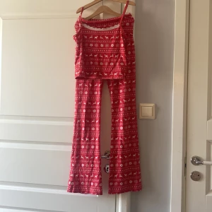Röd julig linnetopp från Gina Tricot - Supermysig röd pyjamassett från Gina Tricot med vitt julmönster av snöflingor, granar och renar. Toppen har smala axelband och spetsdetalj vid halsen och byxorna har yougapans    form. Perfekt för dig som vill ha en festlig vibe under vintern och julen!