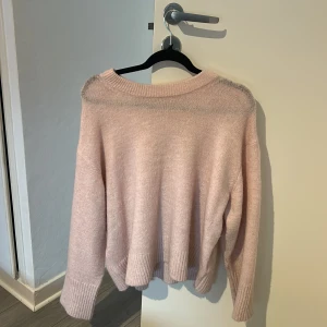 Ljusrosa stickad tröja med ribb - Mysig ljusrosa stickad tröja med bred ribbad kant vid ärmslut och nederkant. Tröjan har en avslappnad passform och långa ärmar, perfekt för kyliga dagar. Enkel och stilren design som är lätt att matcha med jeans eller kjol.