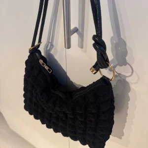 Svart axelväska med gulddetaljer -  Svart axelväska med  guldfärgade detaljer på dragkedjan och ringarna. Använd få tals gånger