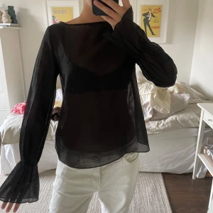 Svart transparent blus med prickar - Säljer en svart transparent blus med diskreta prickar och vida, långa ärmar som har snyggt rynkade muddar. 