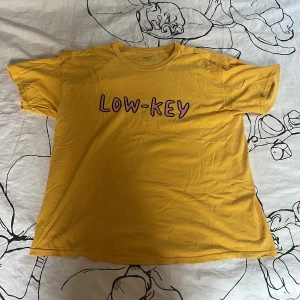 Gul oversized t-shirt Urban Outfitters - Gul t-shirt från Urban Outfitters med oversized passform och trycket 'LOW-KEY' i rosa och svart på bröstet. Klassisk rund hals och korta ärmar. Mjuk bomull som känns chill och skön mot huden, perfekt för en laidback vibe. Inga defekter. Priset kan diskuteras. 