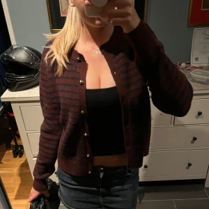 Vinröd och marinblå randig kofta - Säljer en mysig kofta i vinrött med marinblåa ränder 💕 Koftan har lång ärm, rund hals och snygga guldfärgade knappar framtill 🥰Passformen är normal och materialet känns mjukt och sticks inte 🥹 Perfekt att slänga på sig när det är lite kyligt ute 😜 Skriv vid frågor eller prisförslag 💗 (Tröjan är liten i storlek) 