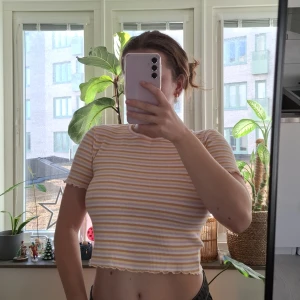 Randig croppad topp från Pull&Bear  - Superfin croppad topp från Pull&Bear med korta ärmar och ribbad struktur. Mönstret är randigt i ljusgult och vitt med vågiga kanter vid ärmslut och nederkant. Aldrig använd så är I superbra skick!😊