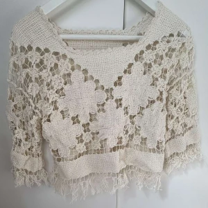 Beige virkad croppad blus med fransar - Superfin beige virkad blus med croppad passform och trekvartsärm. Blusen har ett unikt blommigt mönster och fransar längs nederkanten. Perfekt för dig som gillar boho vibes och vill sticka ut med coola detaljer.