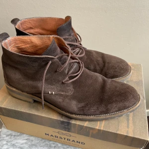 Bruna mockaboots från Marstrand - Snygga bruna boots från Marstrand i mjuk mocka med rund tå och snörning. Insidan är fodrad i ljusbrunt skinn och yttersulan är robust med bra grepp. Perfekt för dig som gillar klassisk stil med en modern touch.