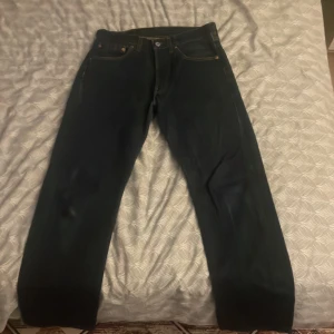 Levi's 501 jeans mörkblå W31 L30 - Säljer ett par klassiska Levi's 501 jeans i mörkblå denim. Modellen har rak passform, fem fickor och snygga kontrastsömmar. Ikonisk läderpatch baktill och röd Levi's-tag på bakfickan. Tillverkade i 100% bomull, perfekt för dig som gillar tidlös stil.
