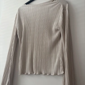 Blus från MQ - Snygg ljusbeige långärmad topp med ribbad struktur och lätt glansig finish. 