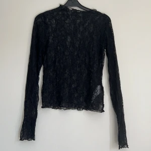 Svart långärmad spetsblus - Säljer en svart långärmad blus i transparent spets med blommigt mönster. Toppen har en slim passform🩶