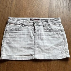 Grå jeanskjol - Lågmidjad ljusgrå jeanskjol med klassiska fem fickor och dekorativa sömmar. Kjolen har en kort passform och är i fint skick! 