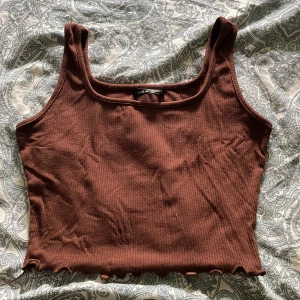 Brun ribbad croppad linnetopp från Shein - Säljer en brun croppad linnetopp från Shein i storlek S. Toppen är ribbad med ärmlös design och har en snygg vågig kant längst ner. Perfekt för dig som gillar enkel och chill stil med lite edge.