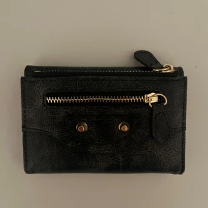 Svart plånbok med gulddetaljer - Snygg svart plånbok i skinn med dragkedja framtill. Insidan har flera kortfack och ett fönster för ID eller foto. Helt ny, aldrig använd. 