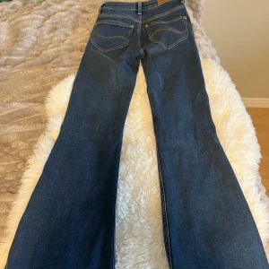 Blå bootcut jeans med utsvängda ben - Säljer ett par klassiska blå jeans med bootcut och utsvängda ben. Jeansen har fem fickor, snygga kontrastsömmar och normal midja. 