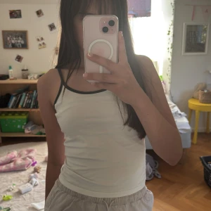 Vit linnetopp med grå kant från H&M - Säljer en enkel och fräsch vit linnetopp från H&M med smala axelband och grå kant runt halsringningen och ärmhålen. Toppen är figurnära och har en clean look som funkar till många olika stilar. Perfekt för dig som gillar minimalistiskt och bekvämt.