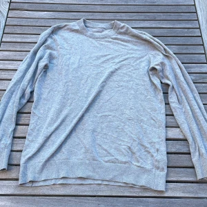 Grå fin långärmad stickad tröja  - En enkel och stilren grå långärmad tröja med rund hals. Tröjan är tillverkad i mjuk bomull och har ribbade muddar vid ärmslut och nederkant. Perfekt för dig som gillar en clean och avslappnad look.