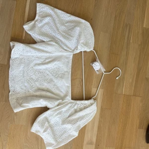 Vit broderad blus med puffärm - Superfin vit blus med breda puffärmar och broderade detaljer. Toppen har ett snyggt hålmönster och är gjord i bomull, vilket gör den både luftig och fräsch. Perfekt för dig som gillar romantisk stil och vill sticka ut med coola detaljer.