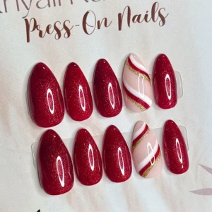 Röda press-on naglar med glitter - Snygga press-on naglar i mandelform med glittrigt röd färg och två naglar med rosa, vita och guldiga swirl-mönster. Perfekt för dig som vill ha en festlig och trendig look utan att gå till salong. Naglarna är av plast och enkla att applicera hemma.