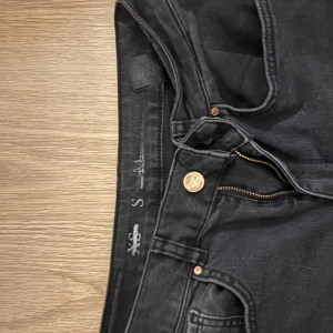 Svarta bootcut jeans XS - Snygga svarta jeans i bootcut-modell med klassisk femficksdesign och guldfärgade detaljer på knappar och nitar. Jeansen har dragkedja och knappstängning, och är tillverkade i mjukt jeansmaterial som sitter skönt. Perfekta för dig som gillar en tidlös look.