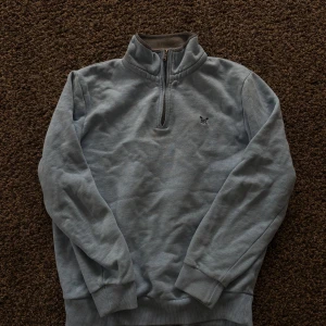 Ljusblå half zip tröja Crew Clothing - Ljusblå långärmad tröja från Crew Clothing Company i storlek S. Tröjan har en ståkrage med half zip-dragkedja och ett litet broderat logomärke på bröstet. Mjuk och skön bomullskvalitet, perfekt för chill dagar. Ribbstickade muddar vid ärmslut och nederkant.