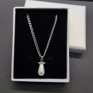 Silverhalsband med pärlhänge - Stilrent halsband i silverfärgad metall med en kedja och ett droppformat vitt pärlhänge. Hänget har en liten detalj upptill som ger extra karaktär. Perfekt för dig som gillar minimalistisk och elegant stil.