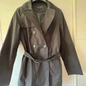 Svart trenchcoat från KappAhl - Snygg svart trenchcoat från KappAhl med klassisk krage, dubbelknäppning och bälte i midjan. Jackan har långa ärmar och är tillverkad i bomull 100% med foder, perfekt för dig som gillar stilrena och tidlösa plagg. Passar dig som vill ha en normal passform. Använd en gång. Dubbelt storlek 40/42