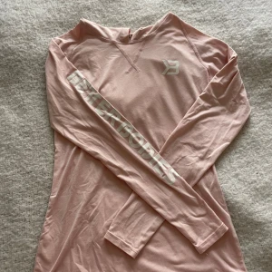 Ljusrosa hoodie från Better Bodies - Säljer en ljusrosa hoodie från Better Bodies i storlek S. Tröjan har långa ärmar, huva och vit logga på bröstet samt texten 'BETTER BODIES' längs ena ärmen. Perfekt för träning eller chill dagar. Materialet är mjukt och känns skönt mot huden.