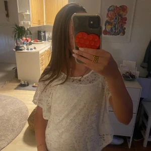 Vit spetsblus från H&M - Säljer en vit blus från H&M med snygg spets och korta, luftiga ärmar. Blusen har en loose passform och är perfekt för dig som gillar romantiska detaljer. Spetsen ger en fräsch och somrig vibe, och den är lätt att matcha med jeans eller shorts.