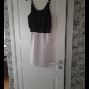 Svart och vit kort klänning med dragkedja - Snygg kort klänning med svart överdel och vit kjol. Kjolen har ett coolt strukturerat mönster och klänningen har smala axelband samt dragkedja i ryggen. Perfekt för dig som gillar kontraster och stilrena detaljer.