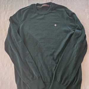 Mörkgrön stickad tröja från Morris - Snygg mörkgrön stickad tröja från Morris i 100% merinoull. Klassisk rund hals och diskret broderad logga på bröstet. Långärmad modell med ribbade muddar vid ärmslut och nederkant. Perfekt för dig som gillar stilrena och tidlösa plagg. Perfekt skick är som ny! Tveka inte med att ställa frågor om det är nåt du undrar!