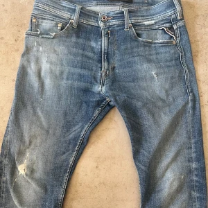 Replay blå jeans med slitningar - Snygga blå jeans från Replay med coola slitningar och lätt tvättad look. Klassisk femficksmodell med Replay-logga på fickan och läderpatch bak. Jeansen har raka ben och normal passform, perfekta för en avslappnad streetstil.