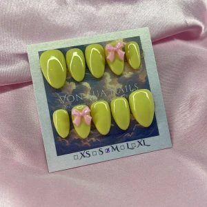 Lemonade (M);Short Almond - Set med handgjorda press-on naglar i en gul färg med glansig finish. Två av naglarna har söta 3D-rosetter i ljusrosa. Naglarna är korta och mandelformade, kommer i M: 16 mm, 12 mm, 12,5 mm, 11,5 mm, 10 mm . Perfekt för dig som vill ha en unik och färgglad look.