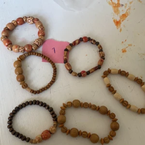 Set med 6 träarmband i olika färger - Säljer ett coolt set med sex handgjorda armband av träpärlor i olika former och färger. Armbanden har naturfärger som beige, brun och inslag av röd, med unika mönster på vissa pärlor. Perfekt för dig som gillar boho eller retrostil och vill mixa och matcha.