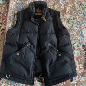 Svart dunväst från Parajumpers XL - Säljer en svart dunväst från Parajumpers Masterpiece Series i storlek XL. Västen har hög krage med gul detalj, två stora fickor med dragkedja och tryckknapp samt robust dragkedja framtill. Perfekt för lager-på-lager och outdoor-vibe. Väldigt bra skick då den knappt har används pågrund av att jag tycker att den är för stor för mig, nypris ligger på 6049kr, hör av er vid frågor och funderingar(: