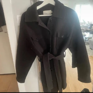 Svart kappa - Stilren svart kappa från NLY Trend med klassisk krage, knappar framtill och två bröstfickor. Jackan har ett matchande bälte i midjan för snygg passform och långa ärmar. Enkel att styla till olika outfits. Lite nopprig💕