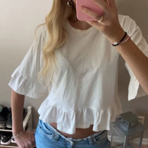 Vit blus med volangdetaljer - Supersöt vit blus med volang längs nederkant och ärmslut, med trekvartsärmar. Som ny💓