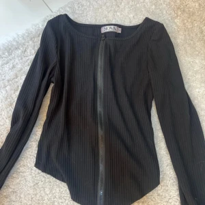 Svart ribbad topp med dragkedja  - Svart långärmad topp från Nova of Sweden i storlek S. Ribbad struktur och hel dragkedja framtill