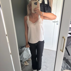 Champagnefärgad linnetopp med spets - Supersöt champagnefärgad linnetopp från Kappahl med tunna axelband och v-ringning dekorerad med spets. Sidenliknande material som ger en lyxig känsla och snygg passform. Perfekt att styla med jeans, kjol eller kostymbyxor. Tyvärr aldrig använt men så fint