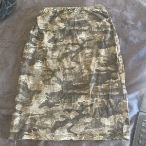 Camouflage mönstrad kjol - Säljer en kjol med coolt camouflage-mönster i olika nyanser av grön, beige och svart. Kjolen har rak passform och resår i midjan för skön komfort. Perfekt för dig som vill sticka ut med en edgy stil.