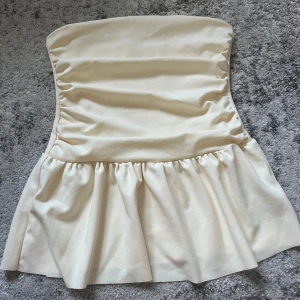 Ljusgul tubtopp från Gina Tricot - Säljer en superfin ljusgul tubtopp som är använd endast en gång. Superfina detaljering volanger. 