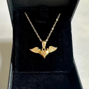 Guld halsband med hjärta💛 - Snyggt halsband i guldton med ett hängsmycke format som ett hjärta med detaljerade vingar på sidorna. 