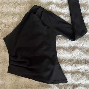 Svart enärmad topp från Gina - Snygg svart enärmad topp från Gina. Den är tajt i armen och går lite ut i midjan. Passar perfekt som festtopp men även till vardags!