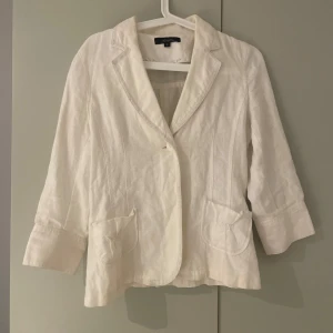 Vit linnekavaj från Twist & Tango - Snygg vit kavaj från Twist & Tango i linne med klassisk krage, trekvartsärmar och dekorativa knappar vid ärmslut. Kavajen har två fickor framtill. 