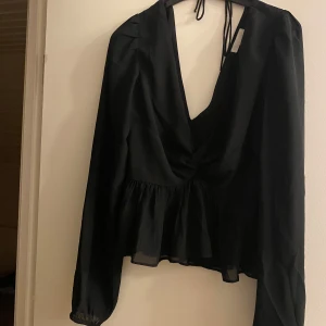 Svart omlottblus med volang från H&M - Supersnygg svart blus från H&M i omlottmodell med djup v-ringning och knyt i nacken. Blusen har långa ärmar med lätt puff och volang nedtill som ger en cool siluett. Ett litet hål vid ryggen men inget som syns/eller tänks på! Köparen står för frakt❣️