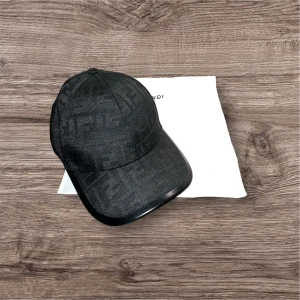 Svart keps från Fendi med FF-mönster - Exklusiv svart keps från Fendi med ikoniskt FF-monogram i ton-i-ton. Klassisk böjd skärm och justerbar passform. Tillverkad i ett stilrent tyg som ger en lyxig känsla. Perfekt accessoar för dig som vill sticka ut med designerstil.
