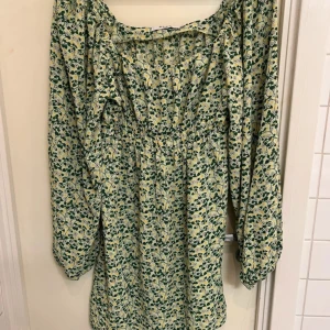 Blommig klänning från NA-KD - Säljer en söt blommig klänning från NA-KD i grönt och gult. Klänningen har långa ärmar och en elastisk midja för en bekväm passform. Perfekt för vår och sommar!