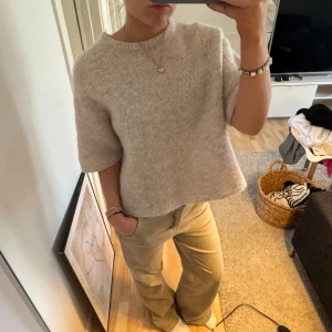 Beige stickad tröja - Säljer en stilren beige stickad tröja med korta ärmar. Perfekt för en avslappnad look. Tröjan har en rund hals och en bekväm passform.